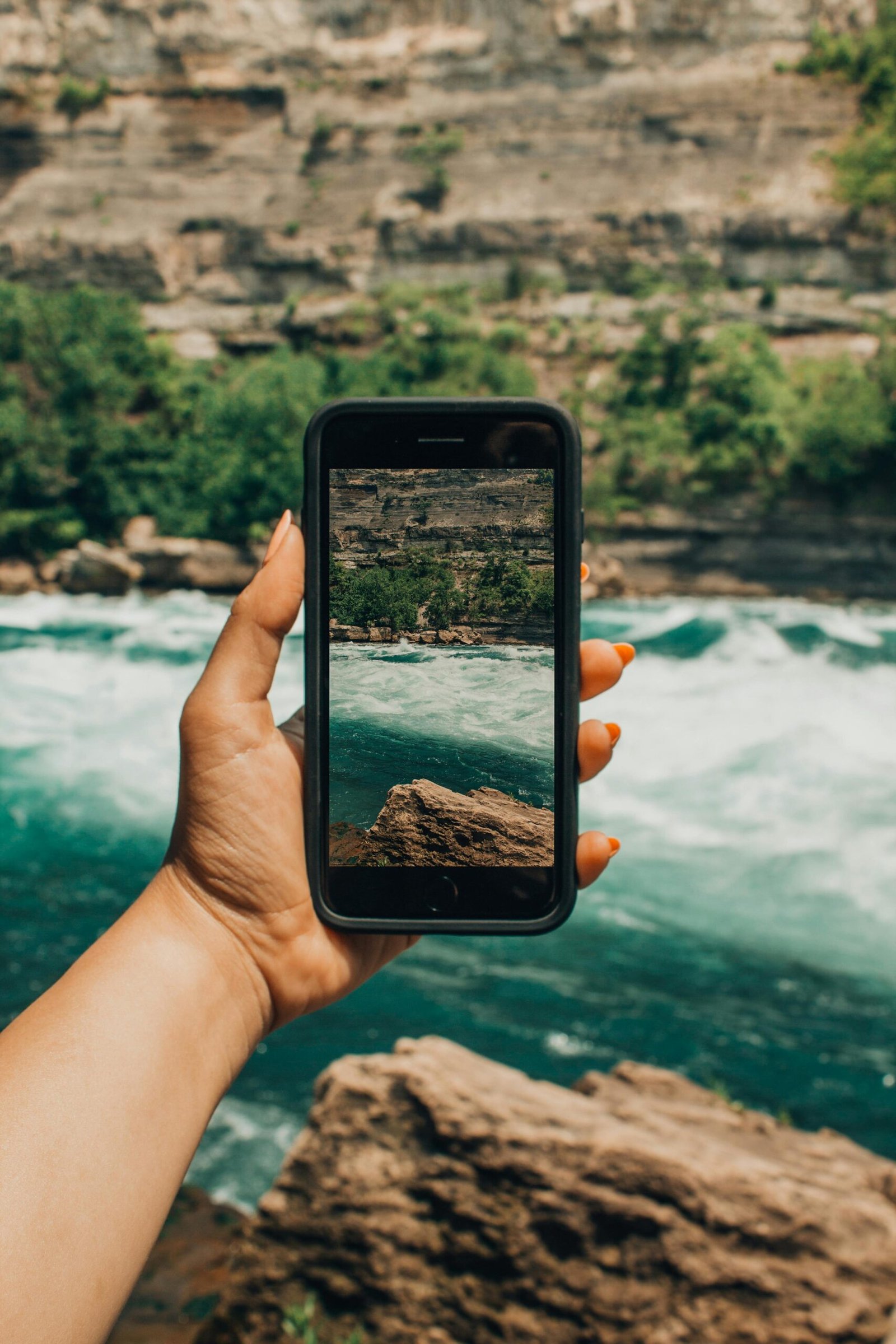 iPhone: o melhor celular do mundo? Hand holding smartphone capturing the stunning view of Niagara Falls rapids.