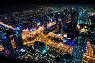 Smart Cities: Como a Tecnologia Está Transformando as Cidades do Futuro A stunning aerial view of Dubai's illuminated skyline at night, showcasing its modern architecture and busy roads.