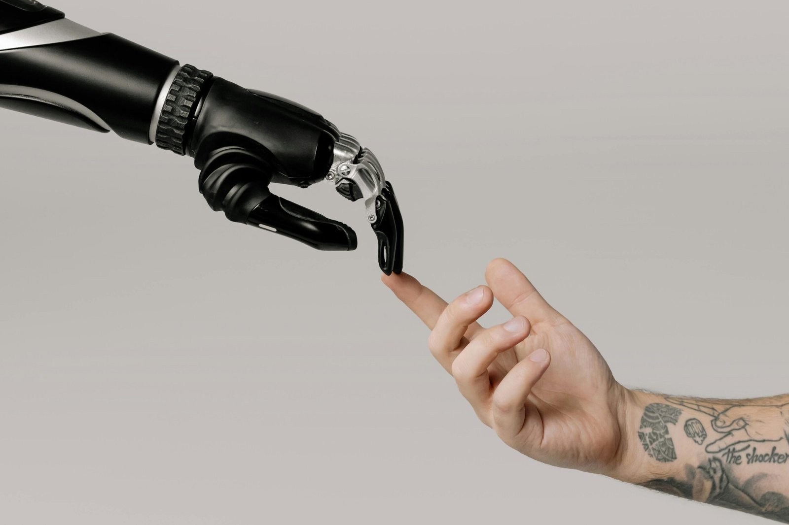 O Futuro é Agora: 7 Usos Práticos da IA Que Você Já Pode Aplicar Hoje. A human hand with tattoos reaching out to a robotic hand on a white background.