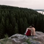 Economia Verde: As Novas Tecnologias Que Estão Criando Oportunidades de Negócio A couple sitting on a cliff, embracing while overlooking a dense forest and lake.