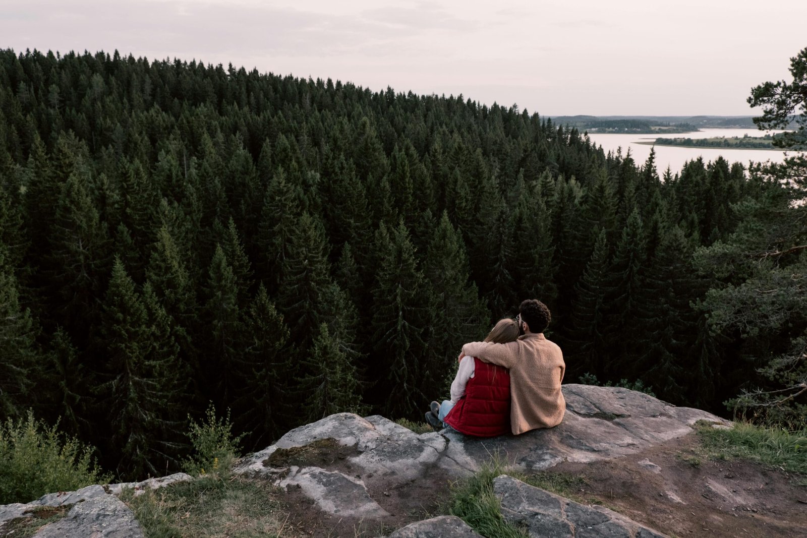 Economia Verde: As Novas Tecnologias Que Estão Criando Oportunidades de Negócio A couple sitting on a cliff, embracing while overlooking a dense forest and lake.
