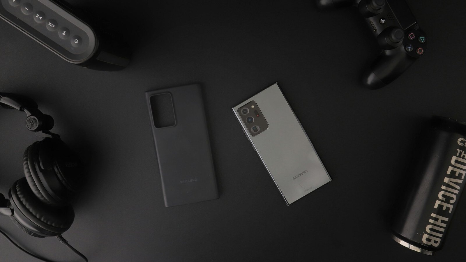 Flat lay of modern electronic gadgets including headphones, phone, and gaming controller on a table.