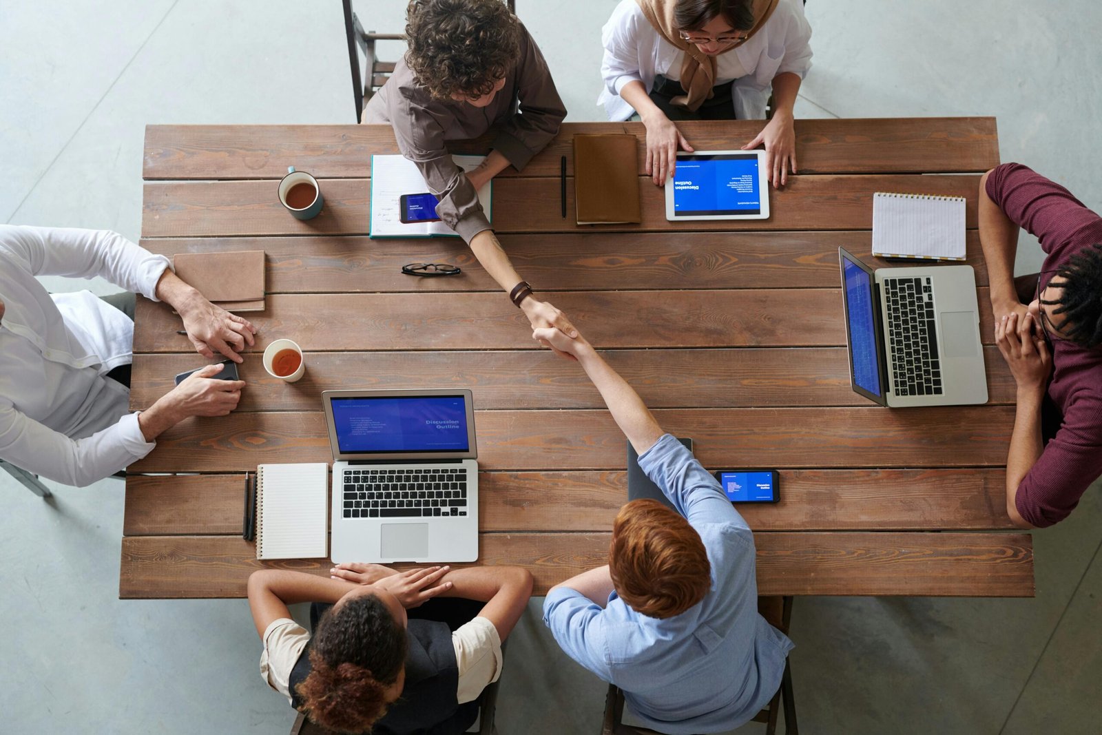 Trabalho Híbrido em 2026, O Novo Normal das Empresas Overhead view of colleagues in a work meeting using laptops and tablets, emphasizing teamwork and technology.